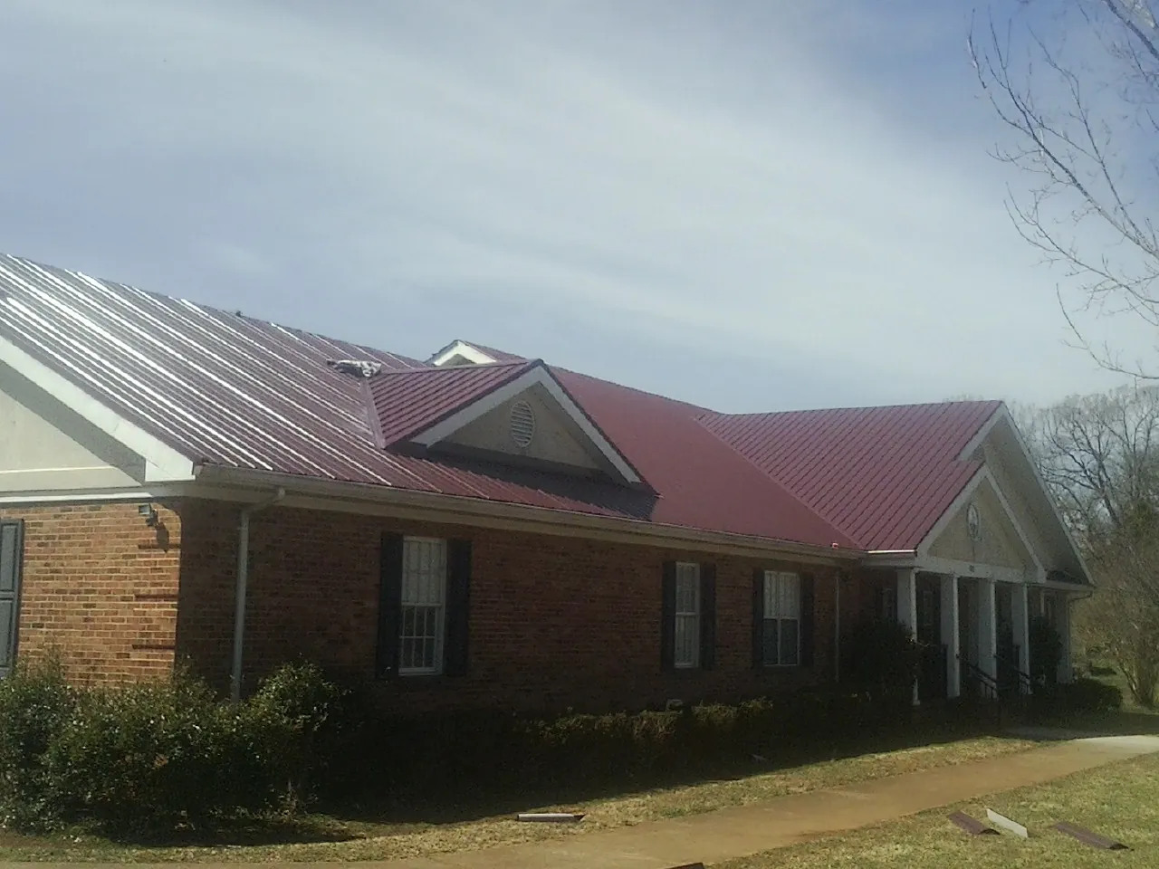 Red metal roof with gabled entries on a long brick building, from a Hail Damage Roof Repair job in Knoxville